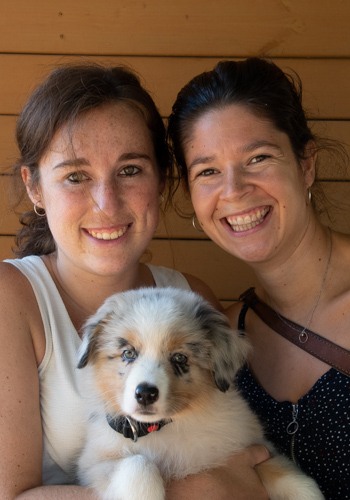 Dues dones somrients amb un cadell d'Australian Shepherd.