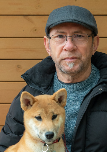 Home amb gos Shiba Inu davant fusta.