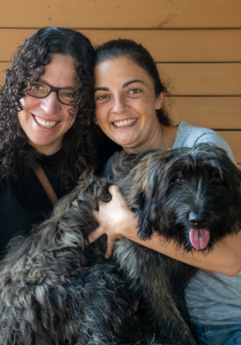 Dues dones somrients amb un gos pelut.