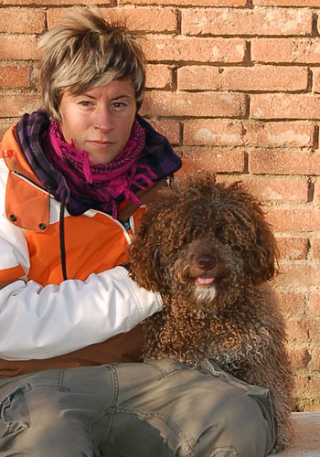 Dona amb gos marró davant d'un mur de maons.