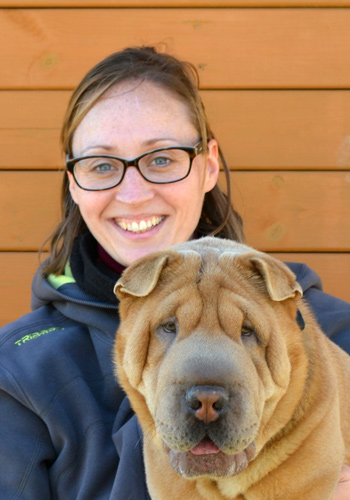 Dona somrient amb gos shar-pei davant d'un fons de fusta.