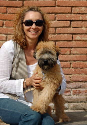 Dona feliç amb gos de raça petit davant paret de maons.