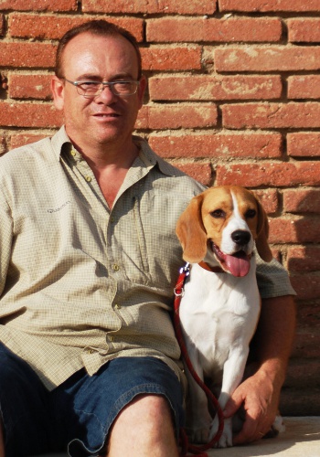 Home assegut amb gos beagle davant de paret de maons.