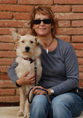 Dona amb gos asseguts davant d'un mur de maons.