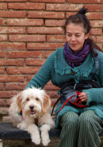 Dona somrient amb gos a banc davant de paret de maons.