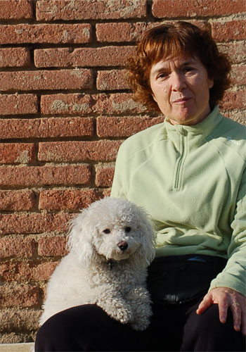 Dona amb gos blanc davant d'un mur de maons.