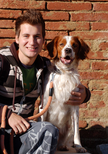 Home jove amb gos davant d'un mur de maons.