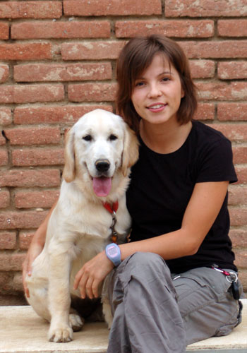 Noia amb gos davant d'un mur de maons.