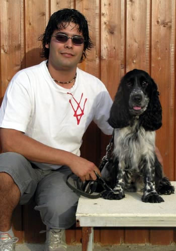 Home assegut amb gos Cocker Spaniel davant fusta.