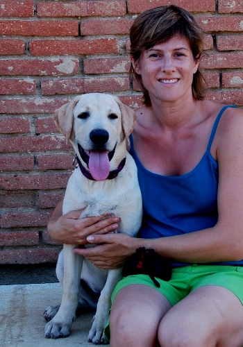 Dona amb gos labrador somrient davant de paret de maons.