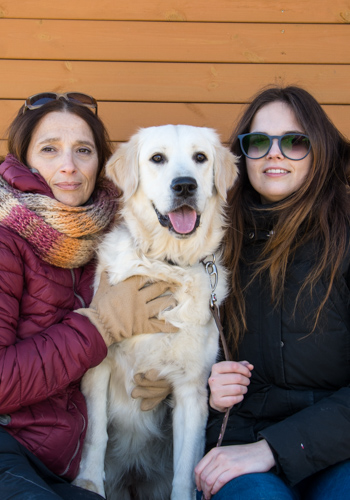 Dues dones i un gos golden retriever somrient.