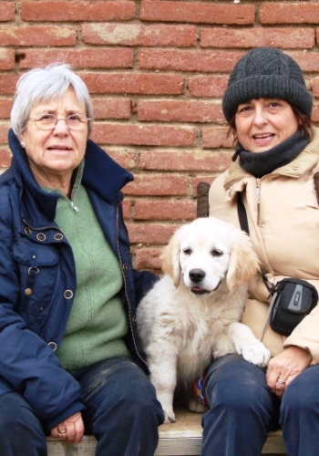 Dues dones i un gosset davant d'un mur de maons.