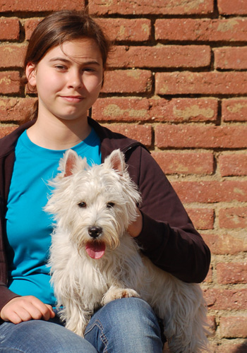 Noia amb gos Westie davant paret de maons.