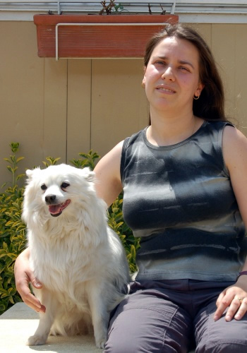 Dona amb gos blanc somrient en exterior.