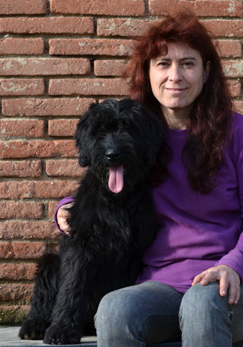 Dona amb gos negre davant paret de maons.