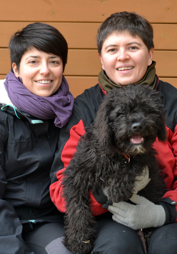 Dues dones i un gos negre somrients.