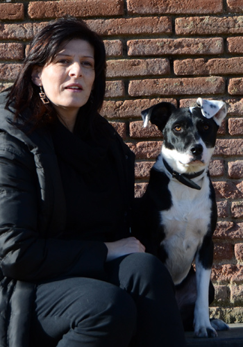 Dona i gos asseguts davant d'una paret de maons.